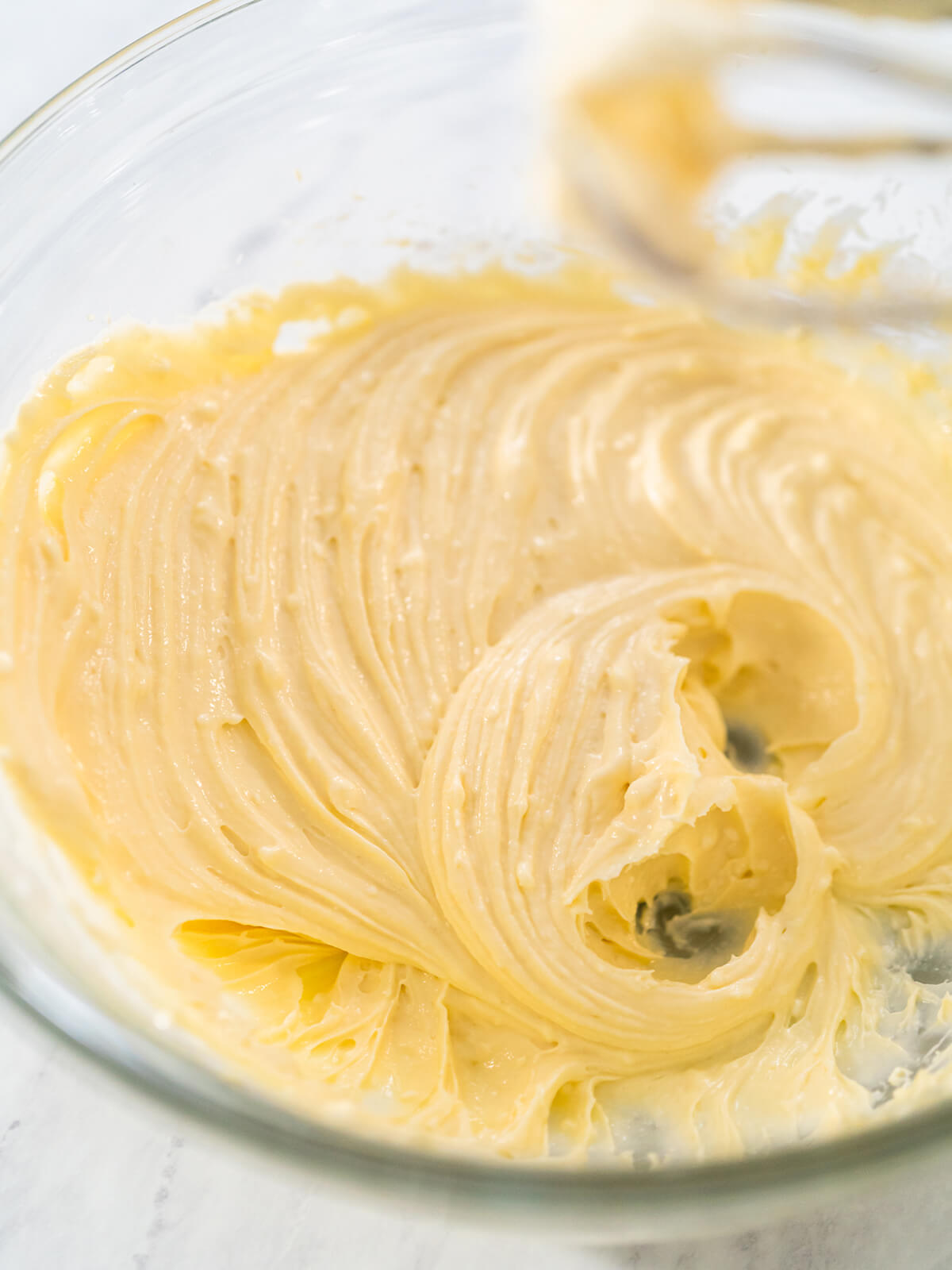 Hellgelbe Frischkäse-Füllung wird in einer Glasschüssel mit dem Handrührgerät glatt gerührt