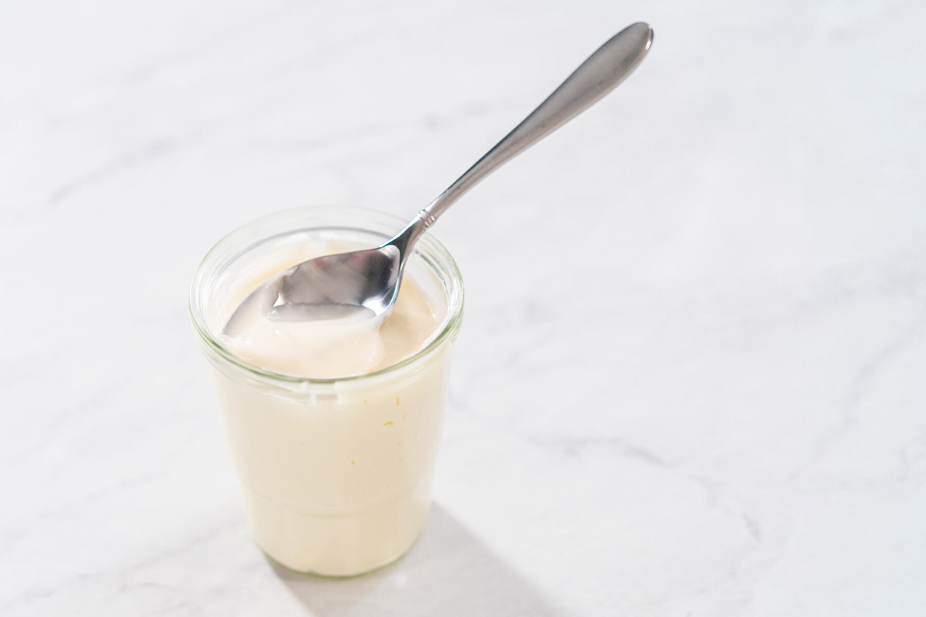 Fertige Frischkäse-Glasur in einem Glas mit einem Löffel darin