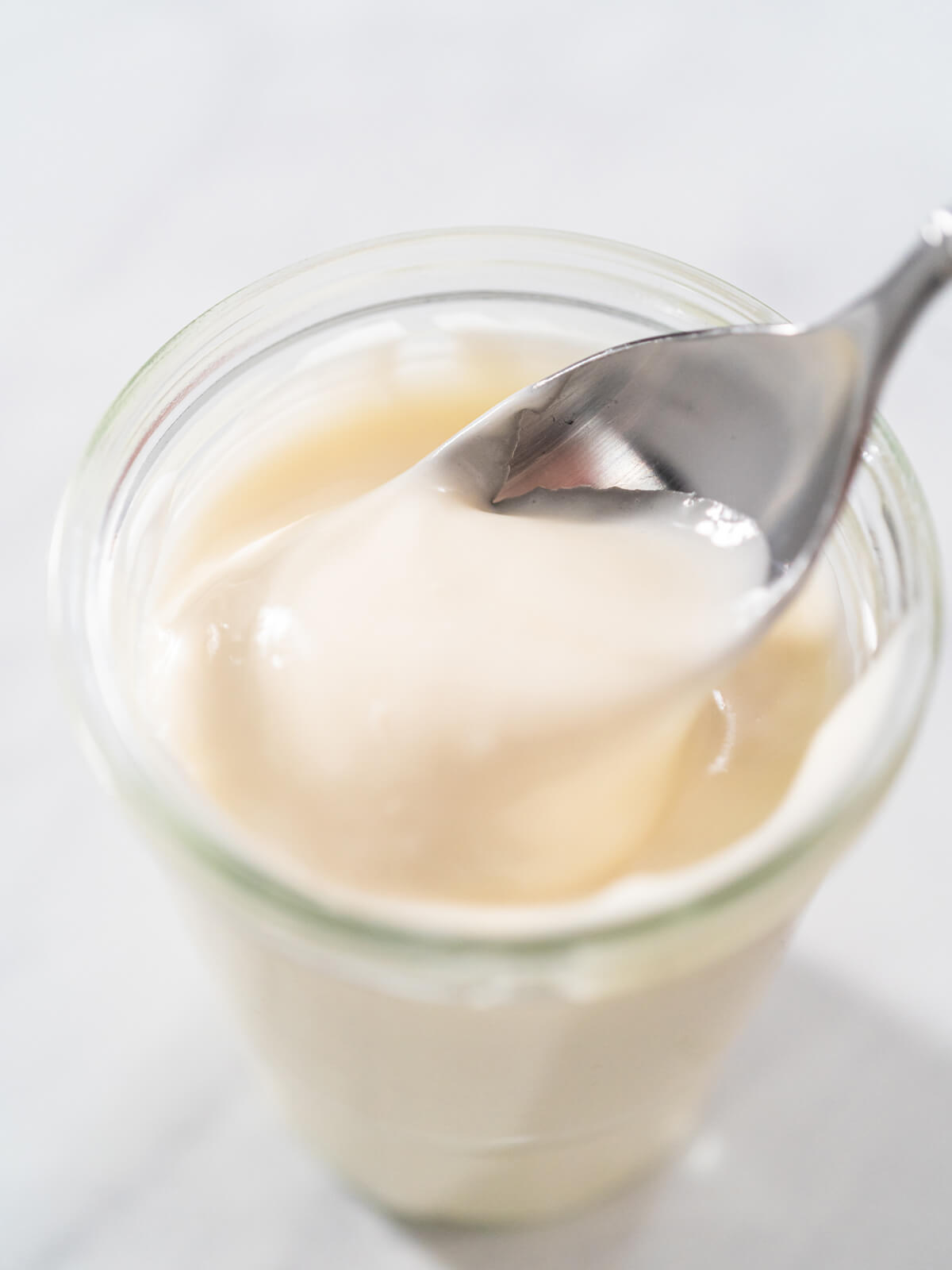 Cremige Frischkäse-Glasur in einem Glas, ein Löffel hebt eine Portion an