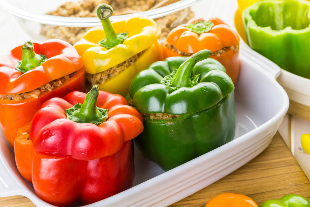 Bunte gefüllte Paprika mit aufgesetzten Kappen stehen dicht aneinander in der Auflaufform, bereit für den Ofen
