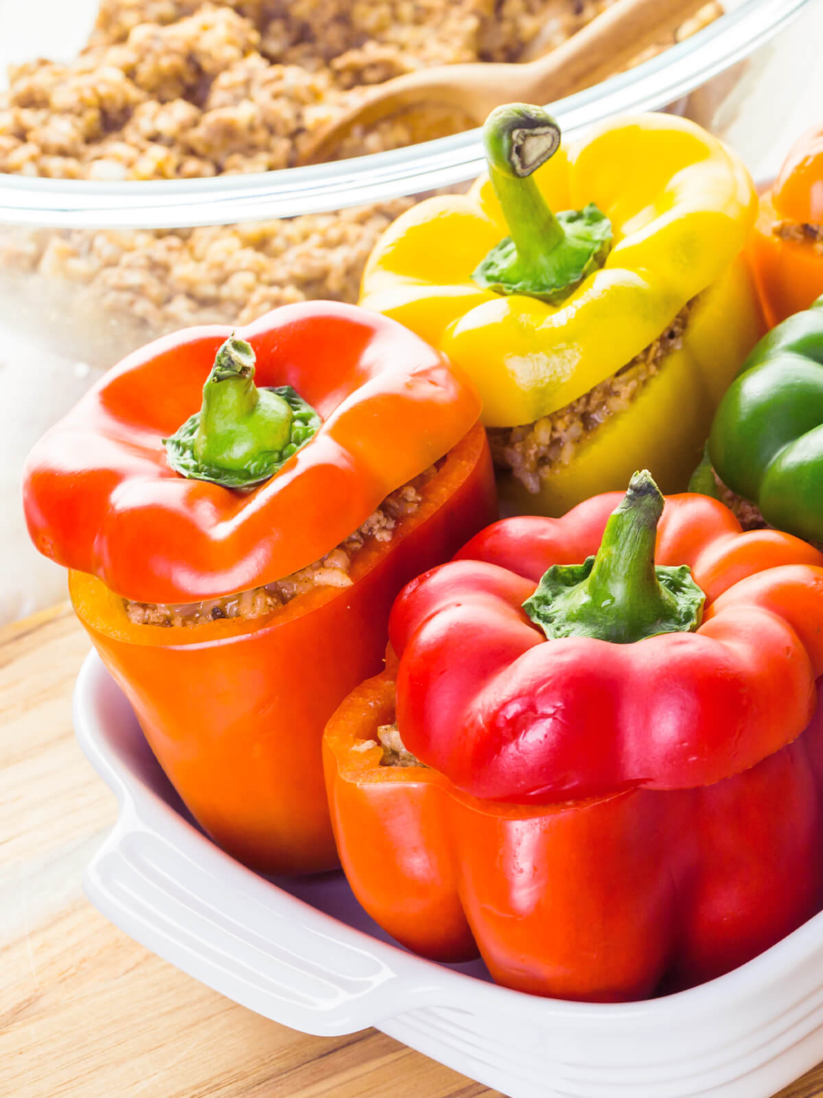 Bunte gefüllte Paprika mit Putenhack und Reis mit aufgesetzten Kappen in der Auflaufform, fertig gefüllt vor dem Backen