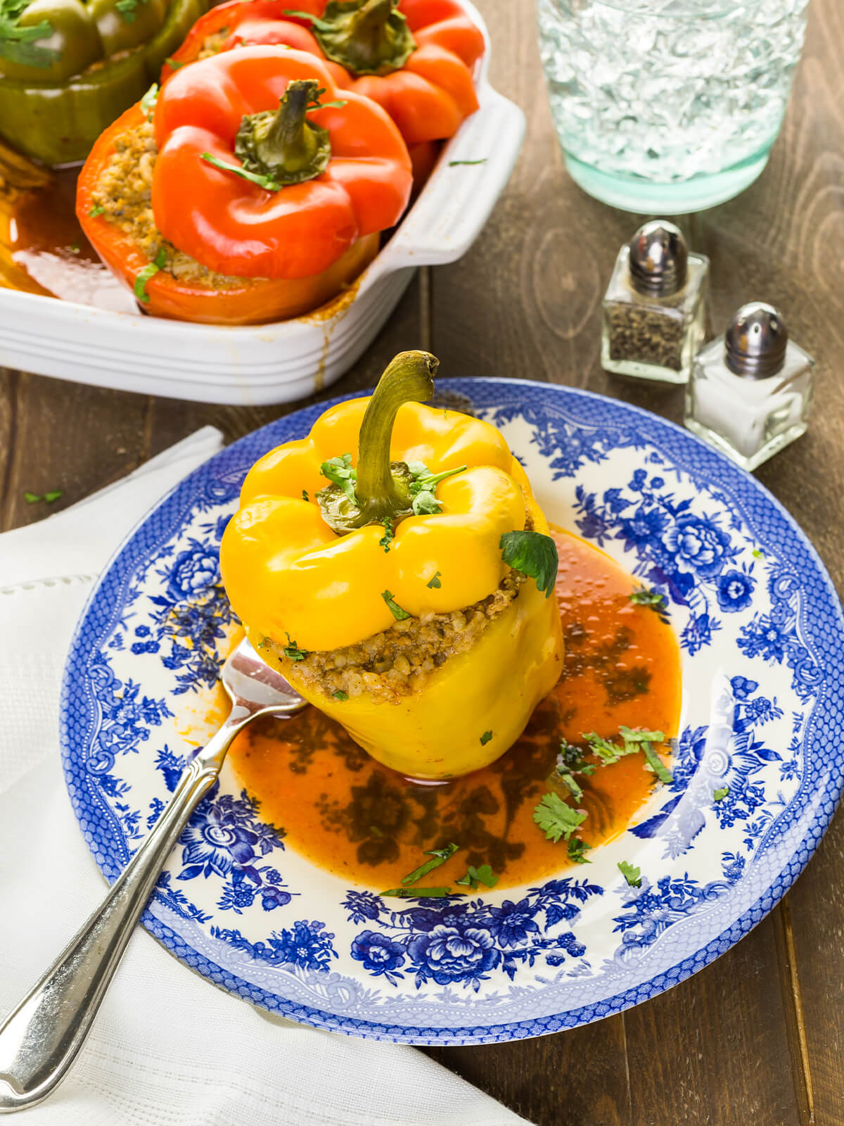 Gebackene gelbe gefüllte Paprika mit Putenhack und Reis auf einem Teller mit rotorangem Sud und Koriandergrün