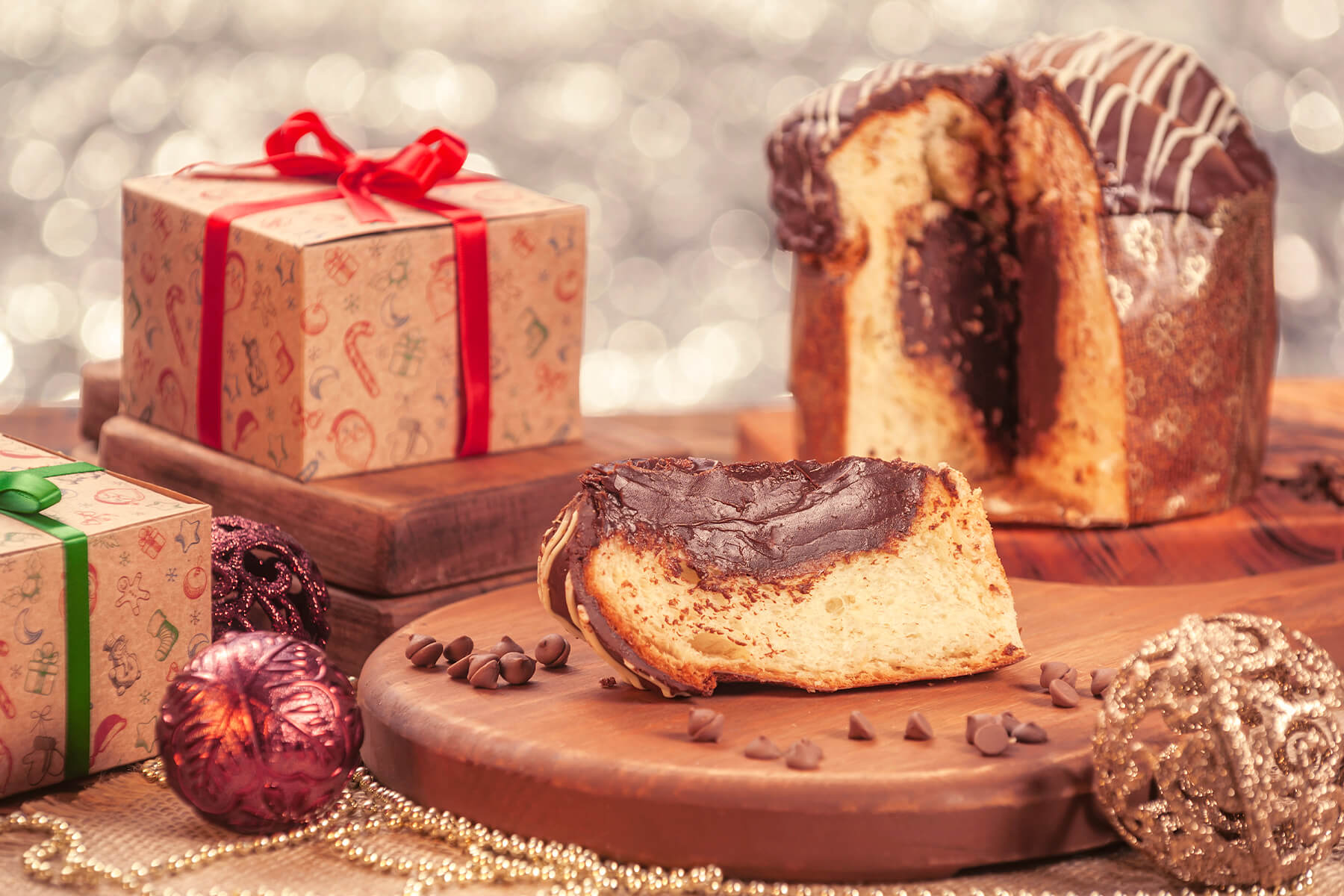 Scheibe eines gefüllten Panettone mit dickem dunklem Schokoladenkern, dahinter der angeschnittene Laib mit weißen Streifen auf der Glasur