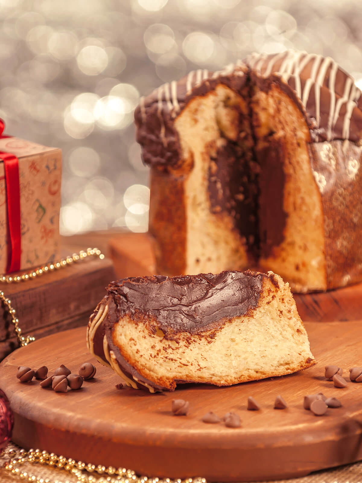 Angeschnittener Panettone mit dunklem Schokoladenkern und glänzender Glasur, davor eine Scheibe auf einem Holzbrett