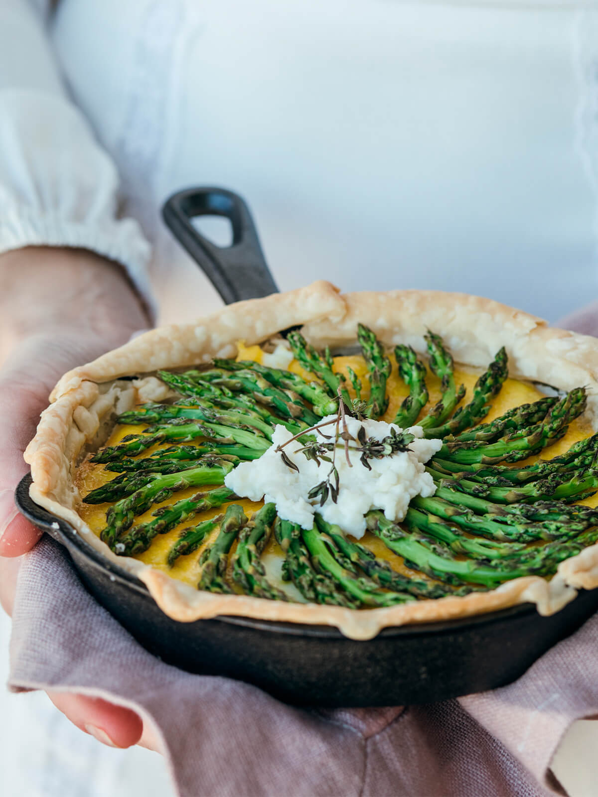 Grüne Spargeltarte mit Safran-Guss und Ricotta-Nocke in einer Gusseisenpfanne, gehalten von zwei Händen