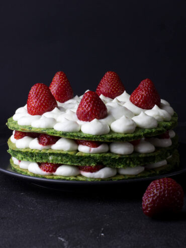 Grüne Schichttorte von der Seite mit drei Böden, weißen Cremetupfen und ganzen Erdbeeren auf der Deckschicht