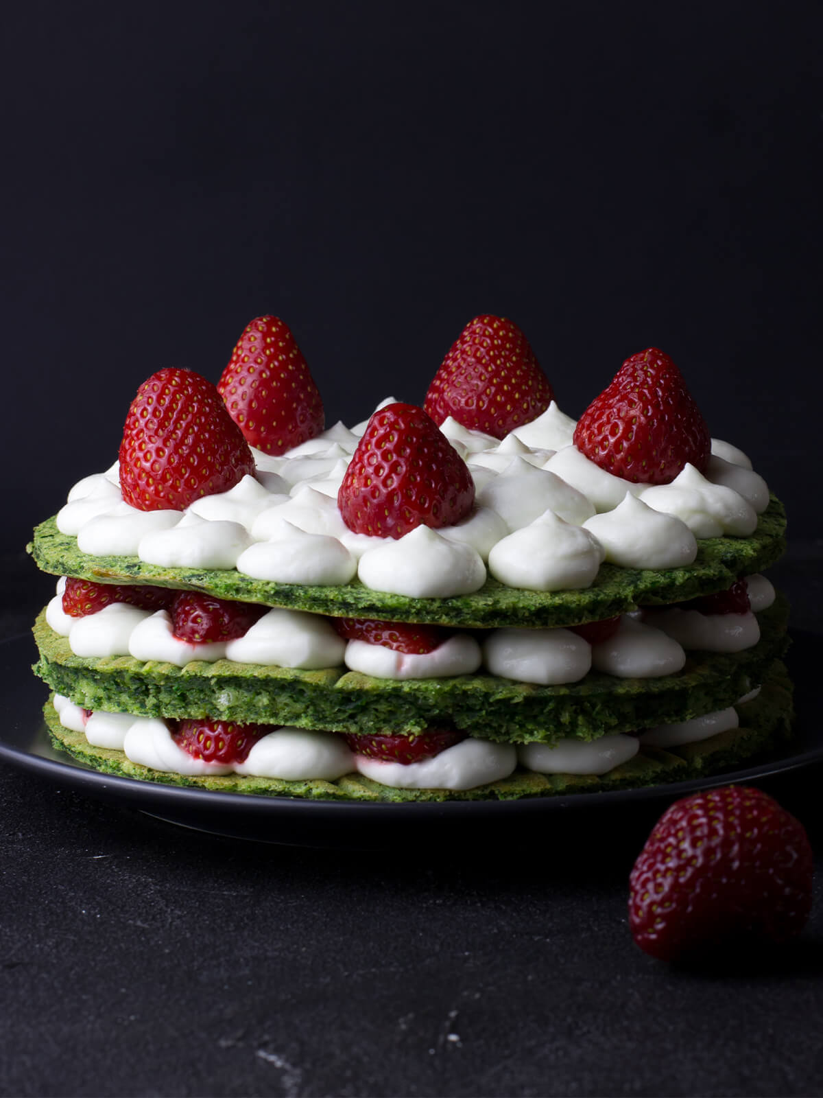 Grüne Schichttorte von der Seite mit drei Böden, weißen Cremetupfen und ganzen Erdbeeren auf der Deckschicht
