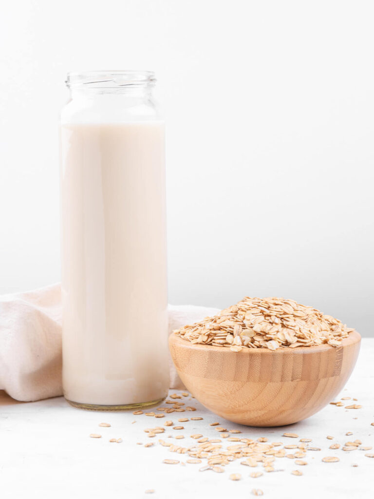 Flasche mit heller Hafermilch neben einer Schale Haferflocken