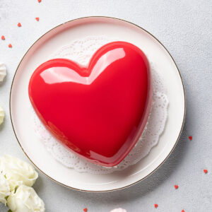 Herz-Mousse-Torte mit spiegelnder roter Glasur auf einem hellen Teller