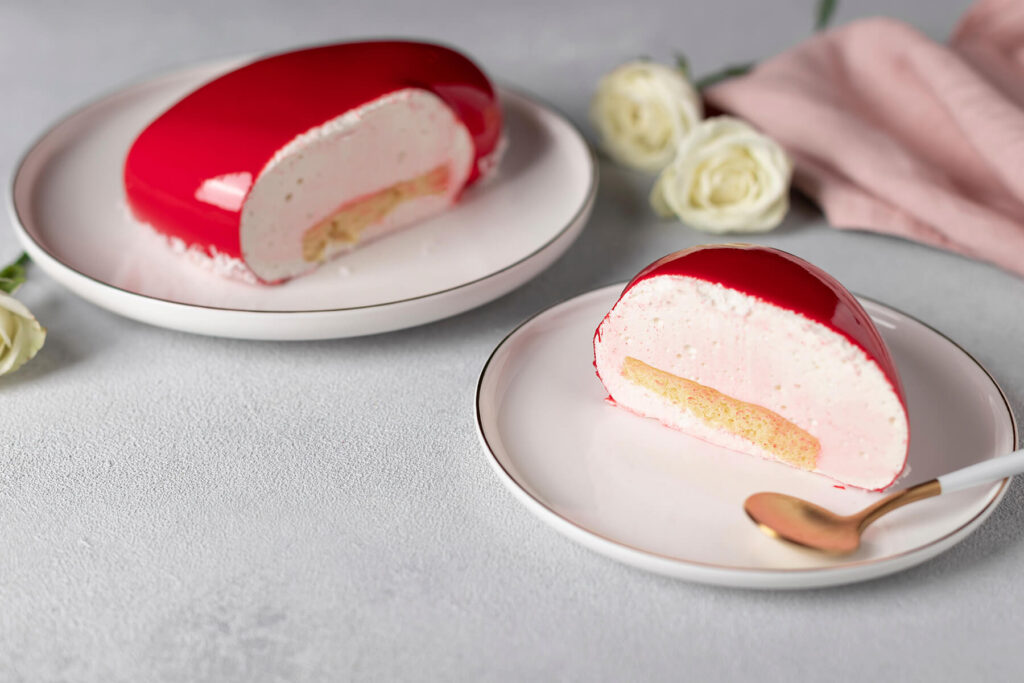 Angeschnittene Mousse-Torte mit roter Spiegelglasur, heller Mousse und dünnem Biskuit