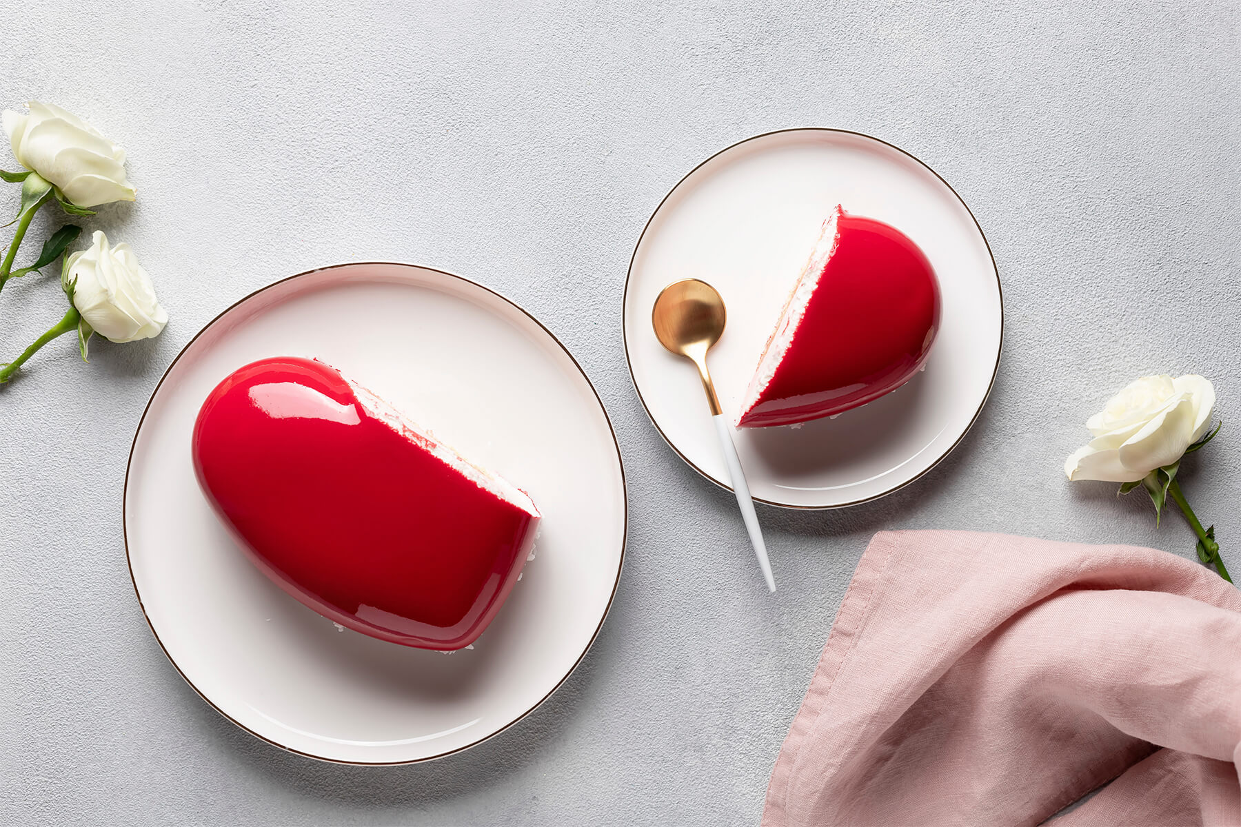 Angeschnittene Herztorte mit roter Spiegelglasur von oben, daneben ein Tortenstück auf kleinem Teller