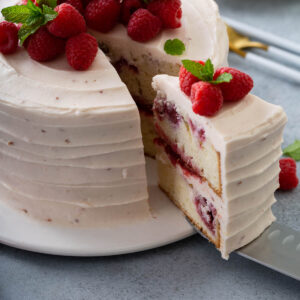Angeschnittene Himbeertorte mit rosa Mascarpone-Creme und frischen Himbeeren auf einer Tortenplatte