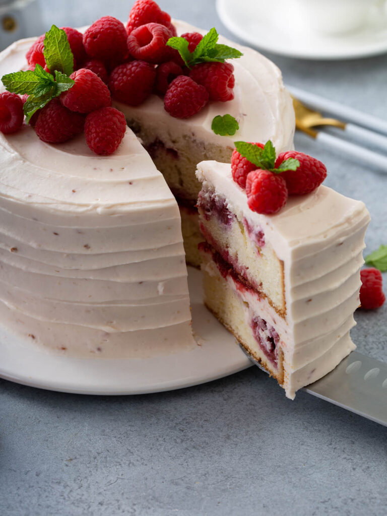 Angeschnittene Himbeertorte mit rosa Mascarpone-Creme und frischen Himbeeren auf einer Tortenplatte