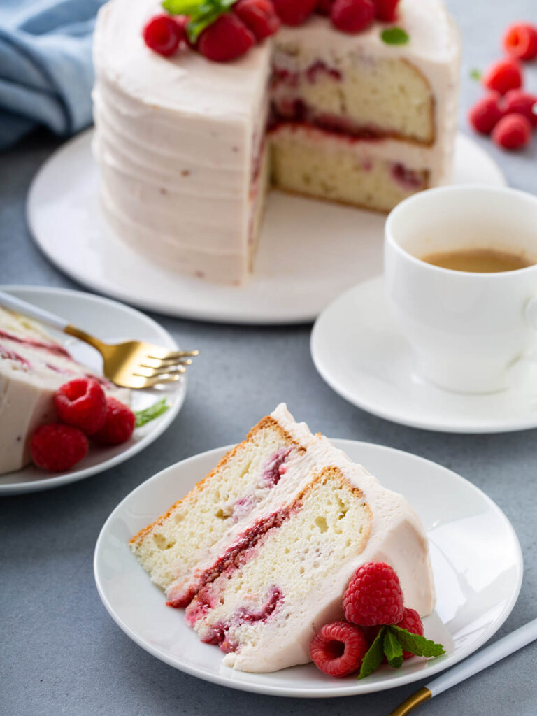 Angeschnittene Himbeertorte mit rosa Mascarpone-Creme, ein Stück auf dem Teller mit frischen Himbeeren und Minze
