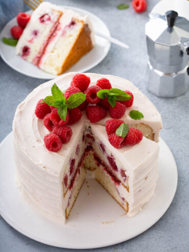 Angeschnittene Himbeertorte mit rosa Mascarpone-Creme, frischen Himbeeren und Minze