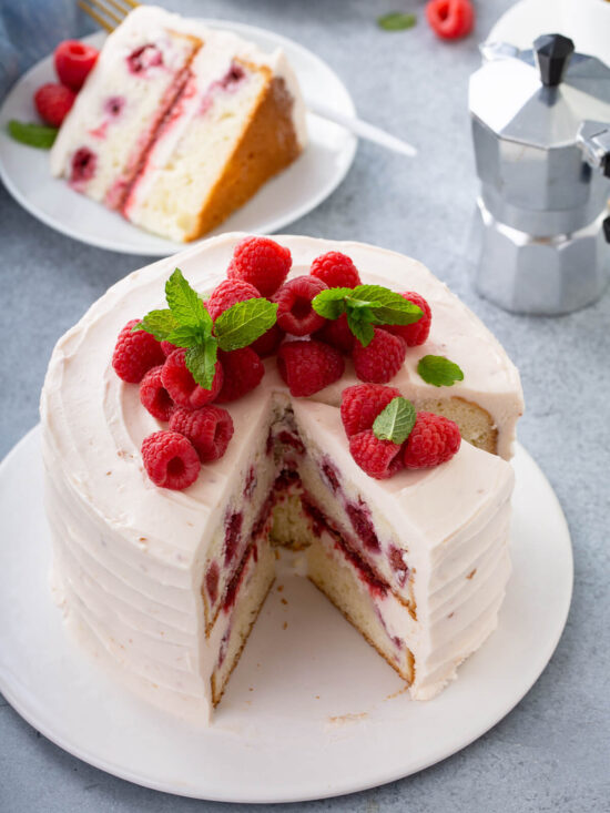 Angeschnittene Himbeertorte mit rosa Mascarpone-Creme, frischen Himbeeren und Minze