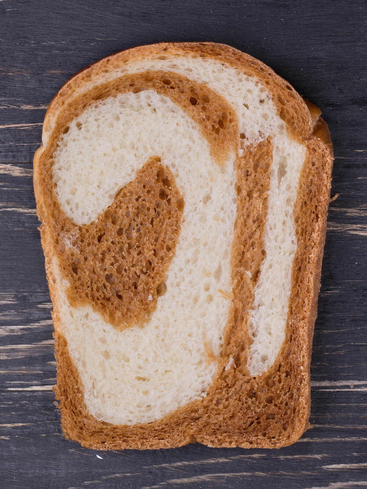 Scheibe japanisches Milchbrot mit Kakao-Marmorierung auf dunklem Holzbrett