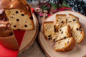 Angeschnittener Panettone auf einem Holzbrett, daneben mehrere Spalten mit kandierten Früchten in der Krume