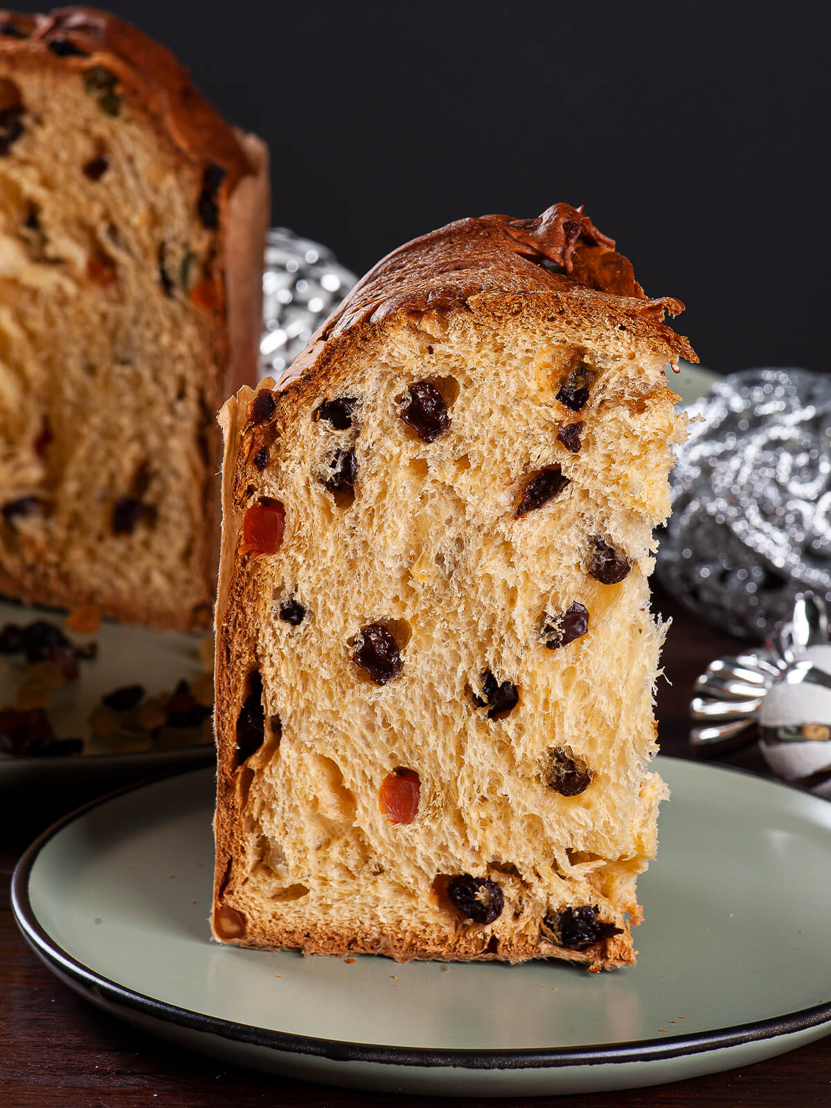 Hohe Scheibe Panettone mit heller, faseriger Krume, Korinthen und kandierten Fruchtwürfeln auf einem grünen Teller