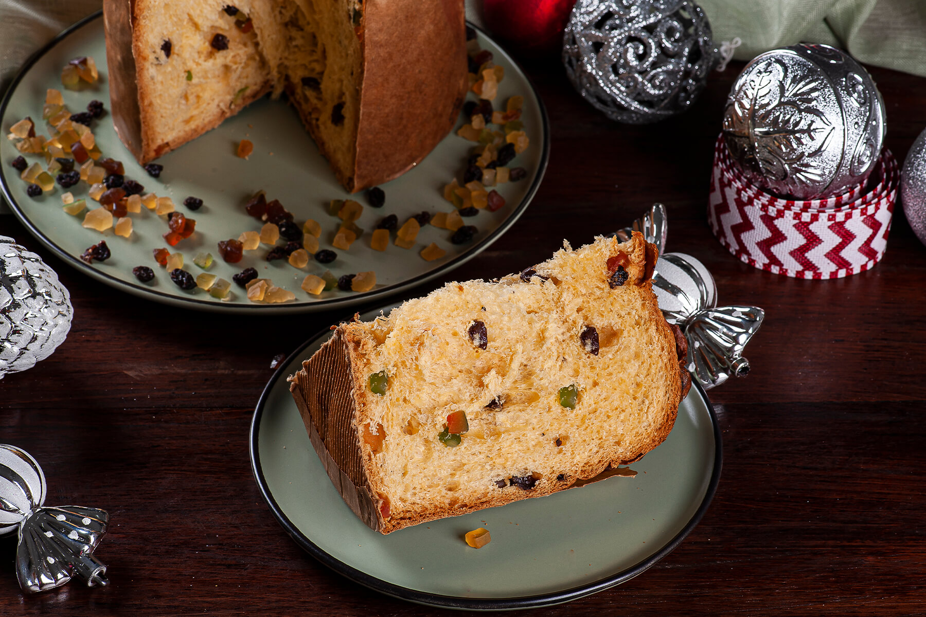 Angeschnittener Panettone auf einem Teller, davor eine liegende Scheibe mit faseriger Krume und bunten kandierten Fruchtwürfeln