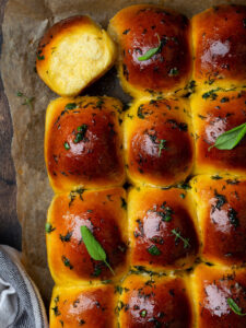 Nahaufnahme eines aufgebrochenen Knoblauchbrötchens mit feiner heller Krume neben glänzenden Brötchen mit Dill-Knoblauch-Butter