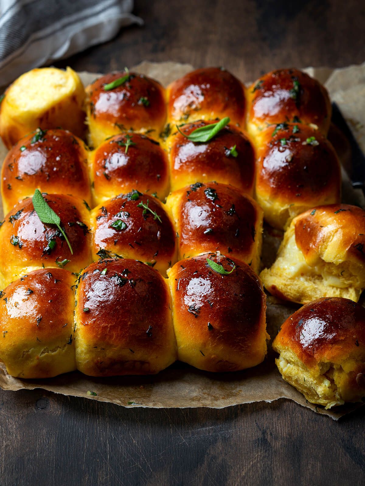 Block aus goldbraunen Knoblauchbrötchen mit Mozzarella-Füllung auf Backpapier, zwei Brötchen aufgebrochen mit geschmolzenem Käse