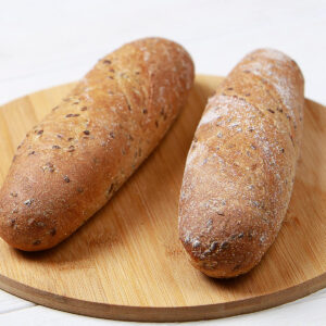 Zwei goldbraune Leinsamen-Baguettes mit Sauerteig nebeneinander auf einem runden Holzbrett