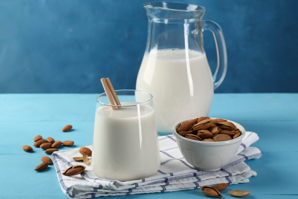 Selbst gemachte Mandelmilch in Glas und Karaffe neben ganzen Mandeln
