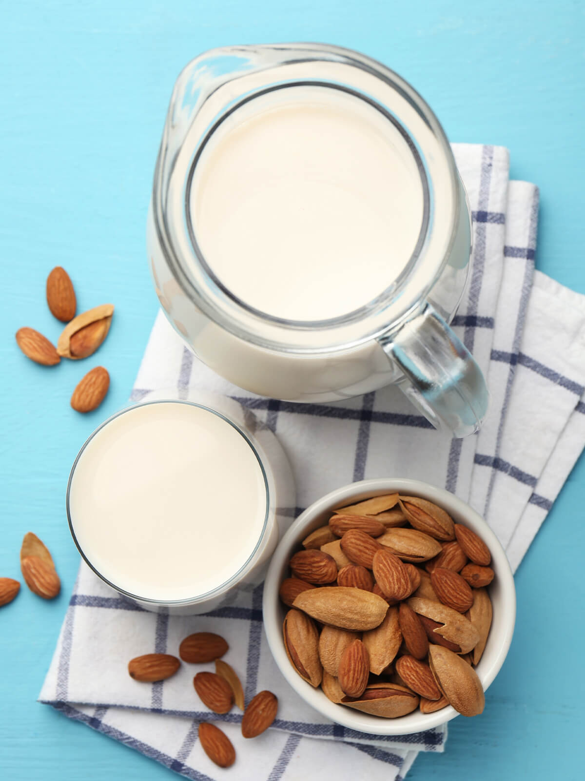 Karaffe und Glas mit selbst gemachter Mandelmilch neben einer Schale Mandeln von oben