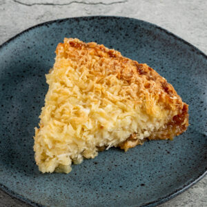Stück Maniok-Kuchen mit Kokos auf blauem Teller, goldbraune Oberfläche und karamellisierter Rand
