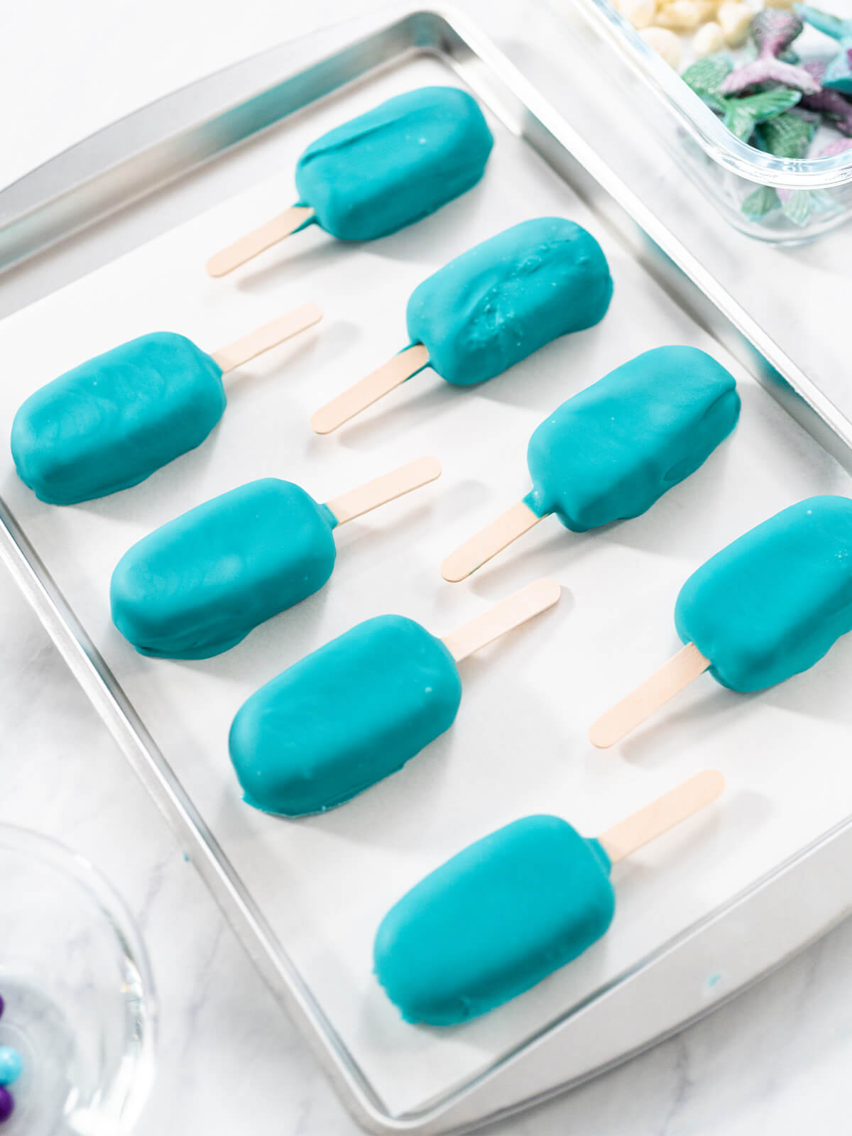 Acht frisch getauchte Cakesicles mit türkiser Glasur auf einem Backblech