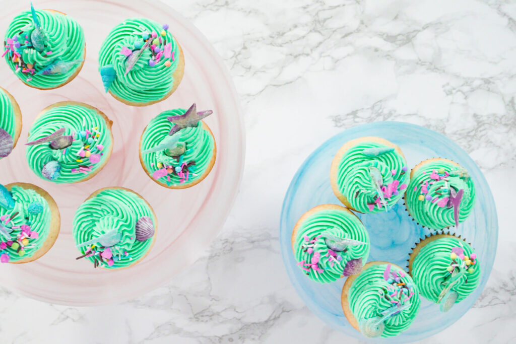 Fertige Meerjungfrauen-Cupcakes mit Flossen und Muscheln auf zwei Tortenplatten