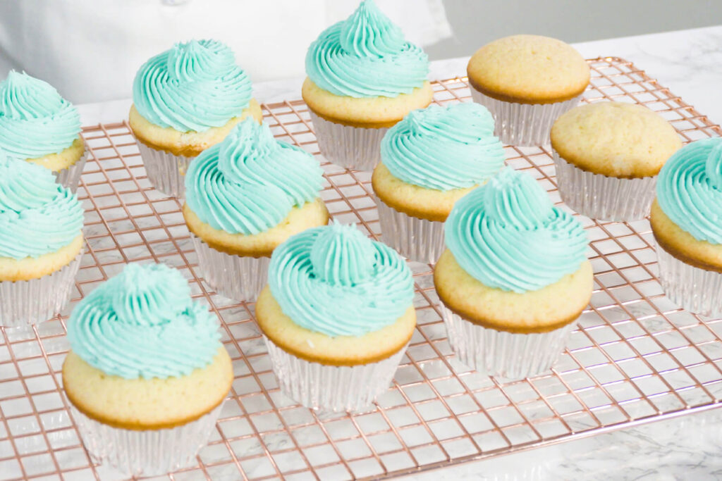 Vanille-Cupcakes mit aufgespritzter türkiser Buttercreme auf einem kupferfarbenen Kuchengitter