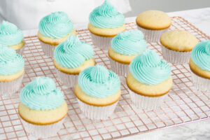 Vanille-Cupcakes mit aufgespritzter türkiser Buttercreme auf einem kupferfarbenen Kuchengitter