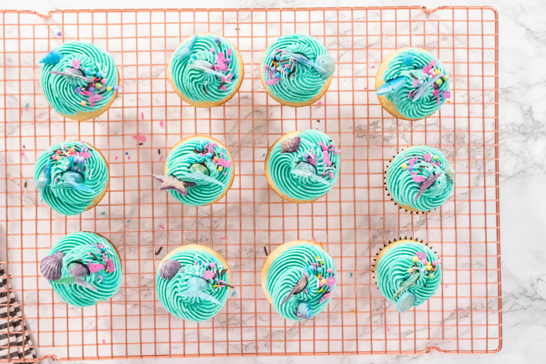 Zwölf fertige Meerjungfrauen-Cupcakes mit türkiser Buttercreme und Flossen von oben auf einem Kuchengitter