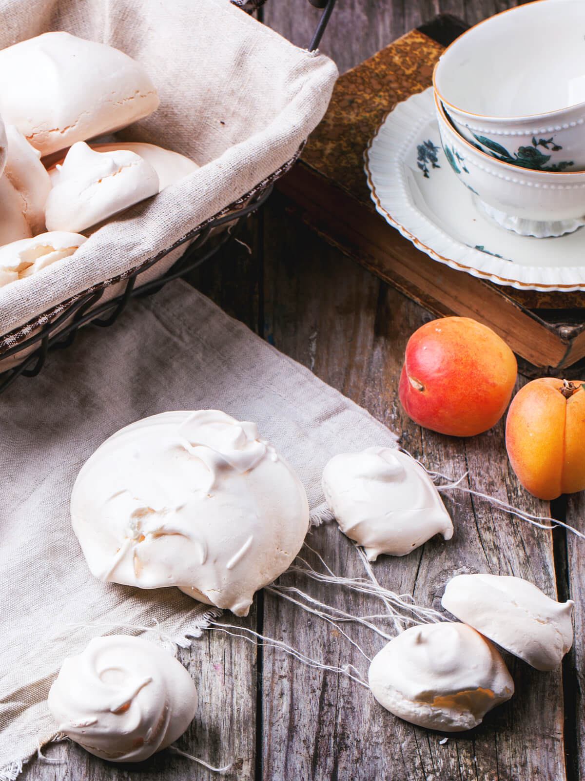 Französische Meringue in drei Größen auf Holz - flache Scheibe, kleine Tropfen und ein Korb voller Baiser