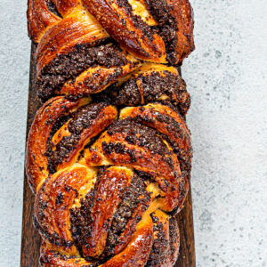 Geflochtene Mohn-Babka von oben mit glänzender Zuckersirup-Glasur auf dunklem Holzbrett