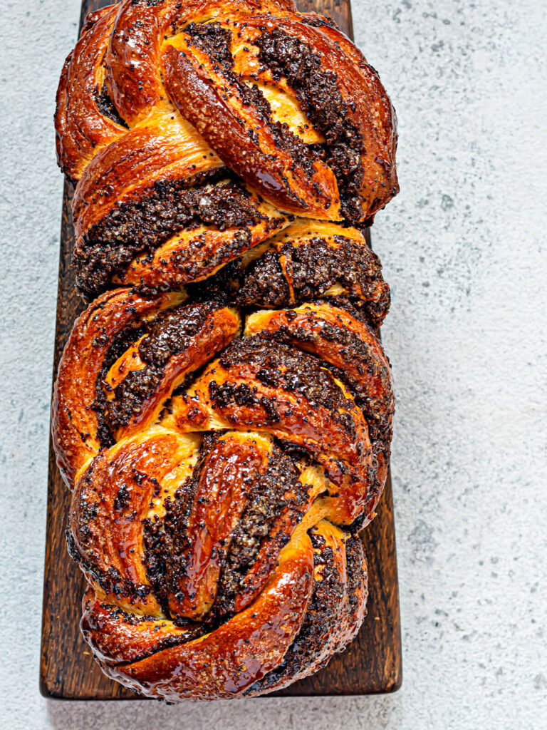 Geflochtene Mohn-Babka von oben mit glänzender Zuckersirup-Glasur auf dunklem Holzbrett