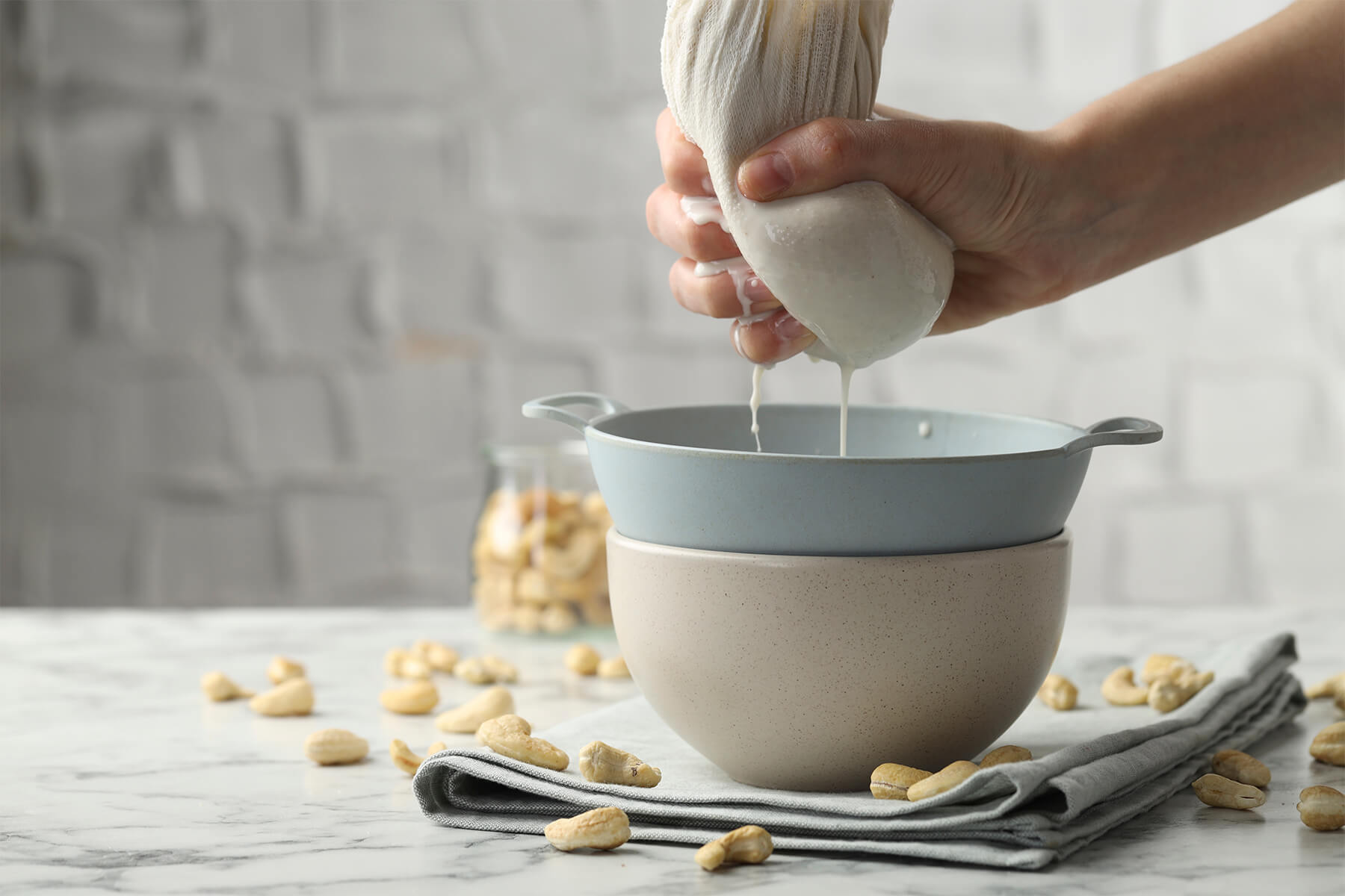 Ein Tuch mit Nusstrester wird über einem Sieb ausgedrückt, darunter läuft weiße Milch in eine Schüssel