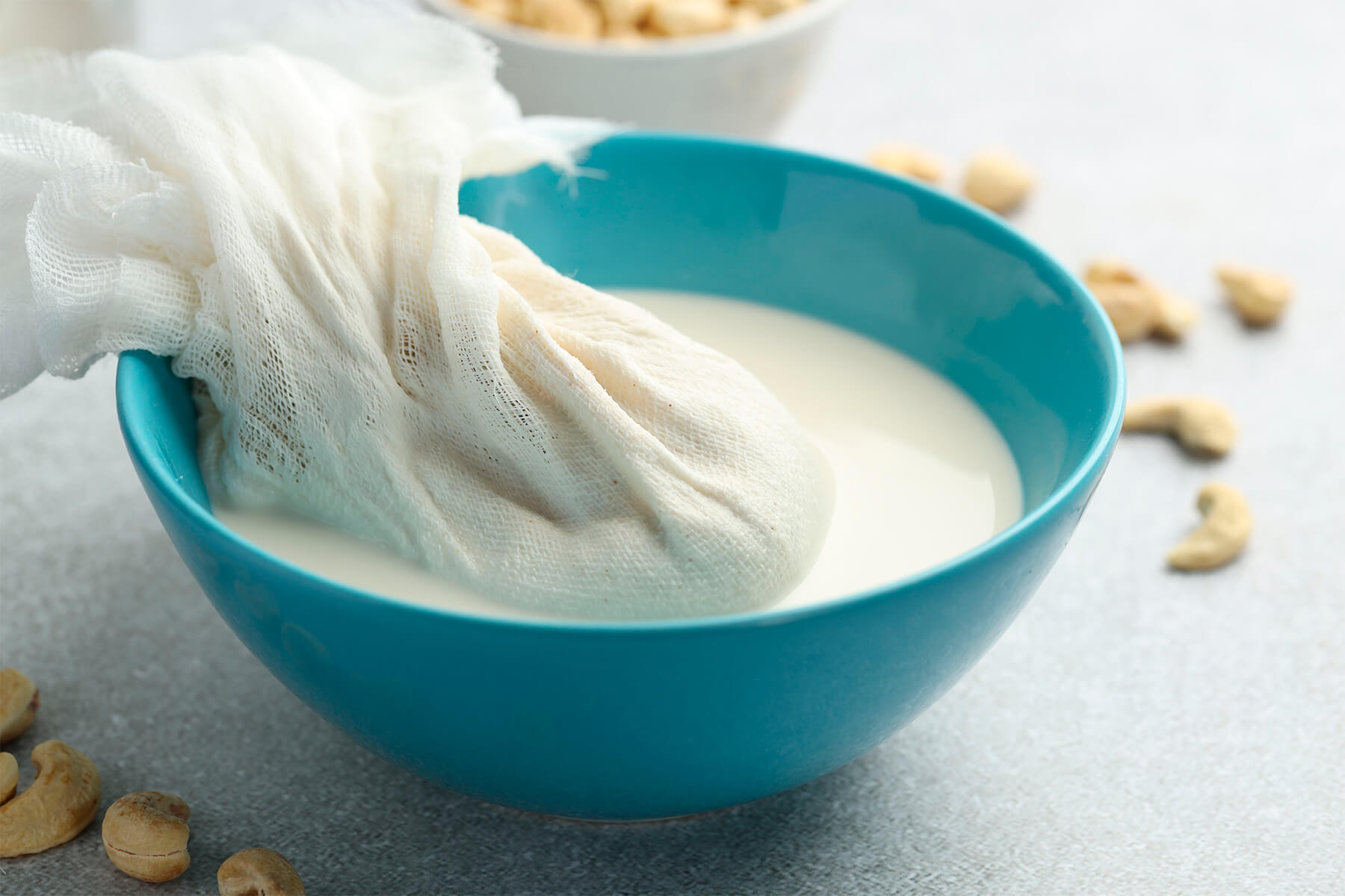 Zusammengedrehtes Passiertuch mit hellem Nusstrester hängt über einer Schüssel mit abgeseihter Milch