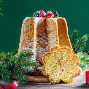 Goldbrauner Pandoro in Achtzackform mit Puderzucker und Beeren, davor eine sternförmige Scheibe mit hellgelber, feinporiger Krume
