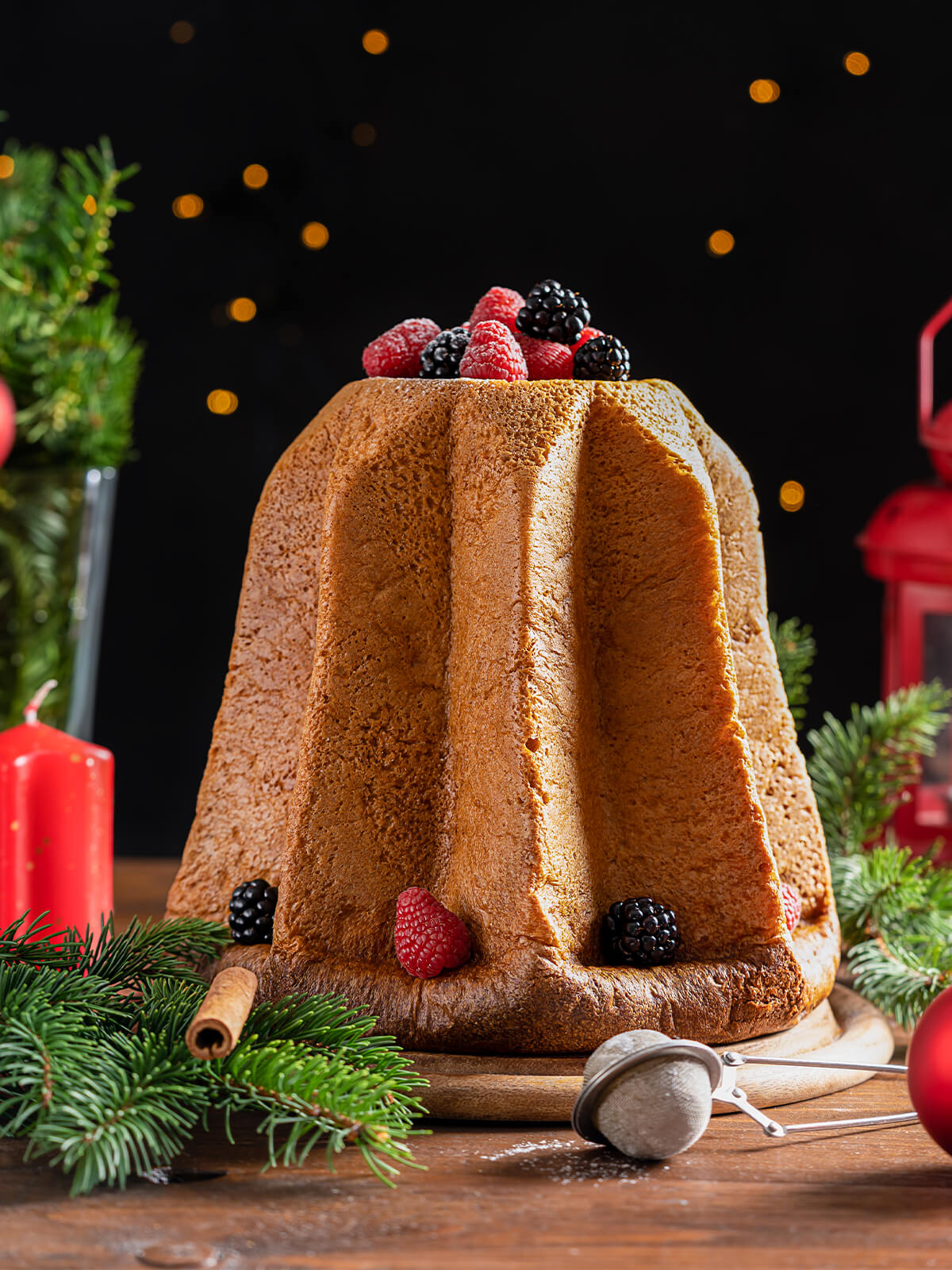 Pandoro in Sternform mit goldbrauner Kruste und tiefen Rillen, obenauf frische Himbeeren und Brombeeren, auf einem Holzbrett