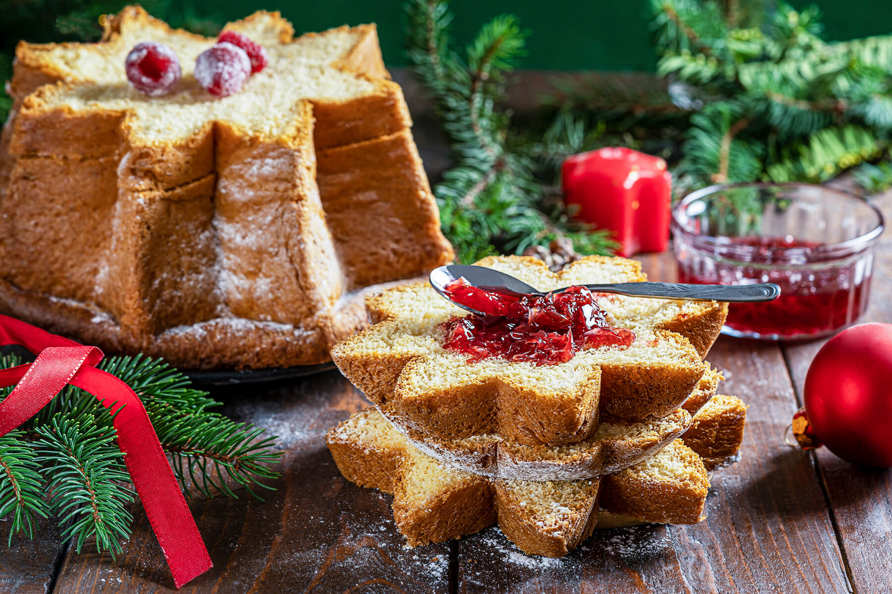Waagerecht geschnittene Pandoro-Scheiben zu einem Tannenbaum aufgeschichtet, jede Lage versetzt, oben mit rotem Fruchtaufstrich und Puderzucker