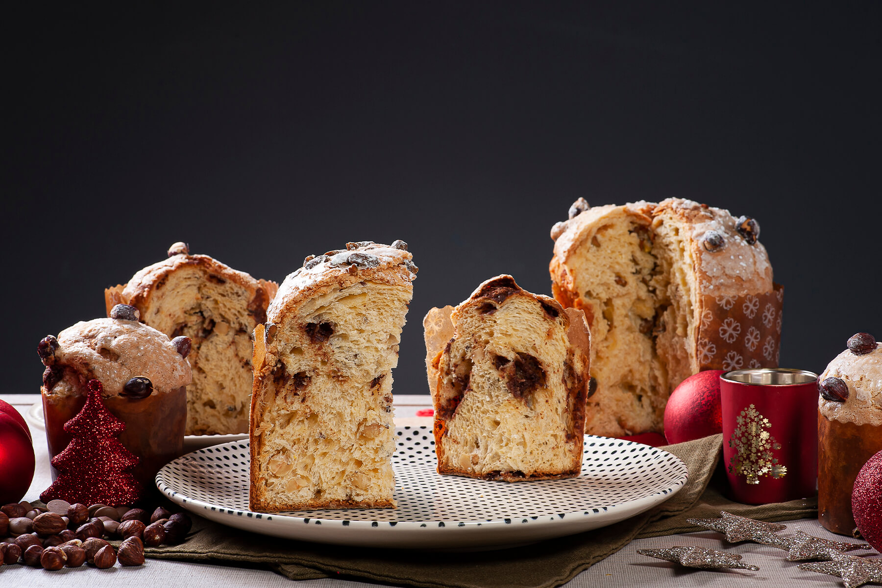 Aufgeschnittene Panettone-Hälften mit dunkler Nougat-Spirale in der hellen Krume, dahinter weitere Laibe mit Nussglasur