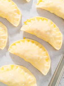 Ungebackene Puten-Empanadas mit Ei bestrichen auf einem Blech mit Backpapier