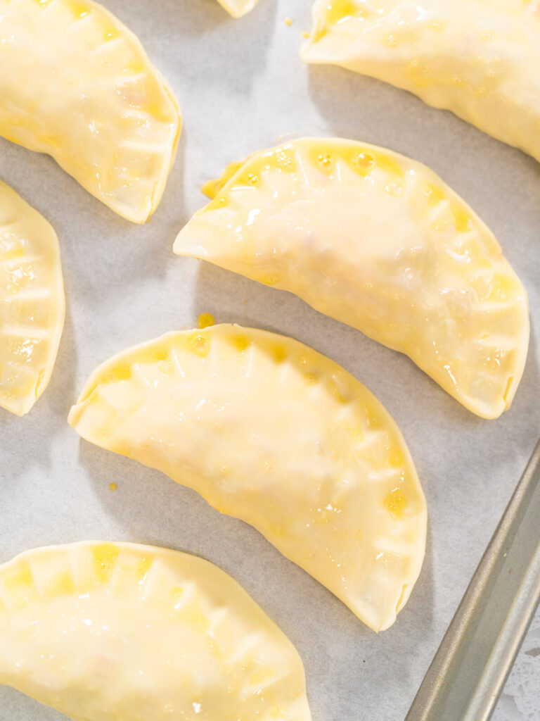 Ungebackene Puten-Empanadas mit Ei bestrichen auf einem Blech mit Backpapier