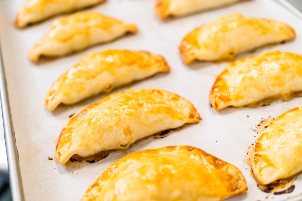 Frisch gebackene Puten-Empanadas mit goldbraunem Rand auf dem Backblech