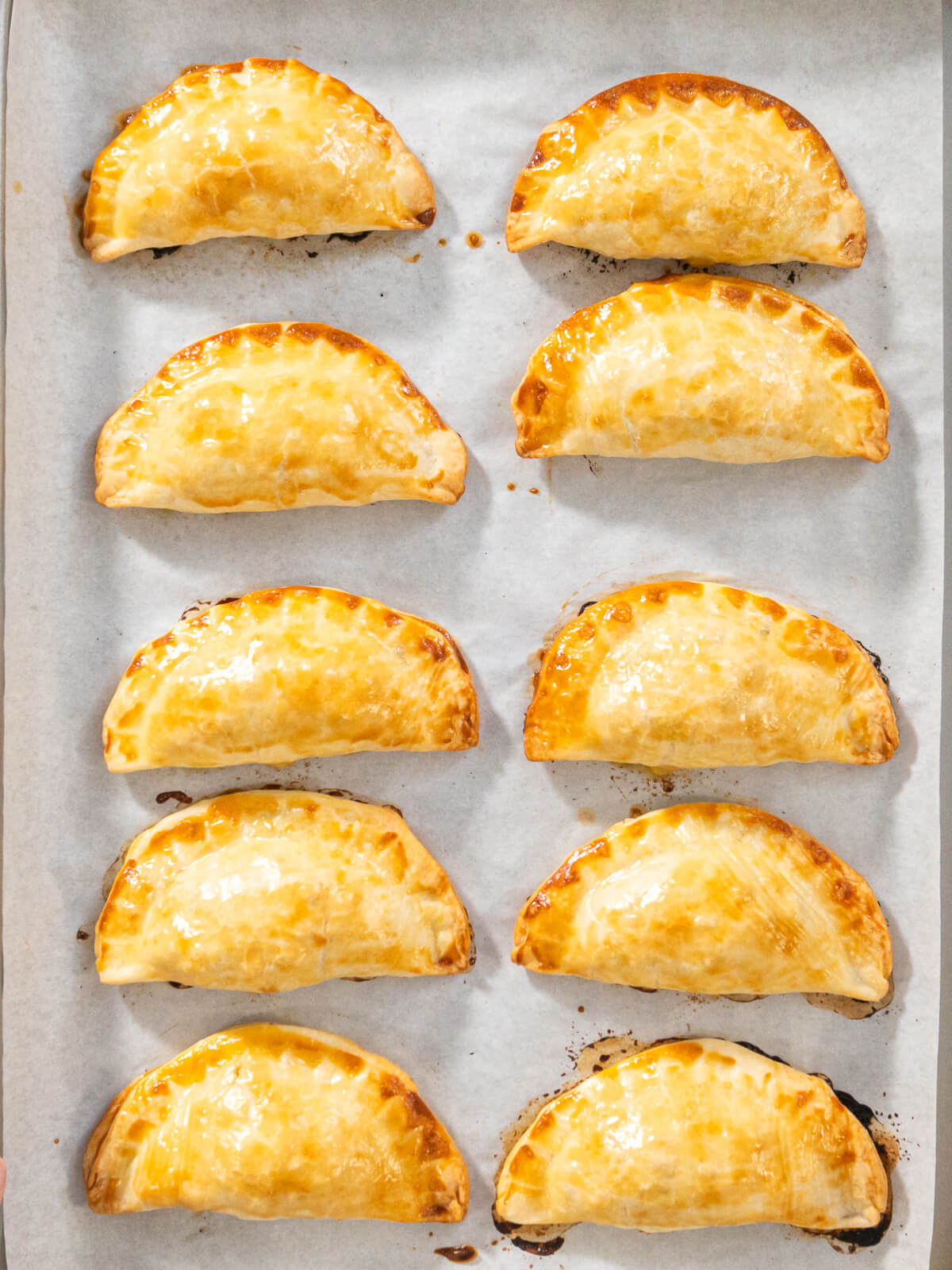 Zehn gebackene Puten-Empanadas von oben nebeneinander auf dem Backblech mit Backpapier