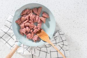 Rohes Putenhackfleisch in Stücken in einer hellblauen Pfanne mit Holzwender