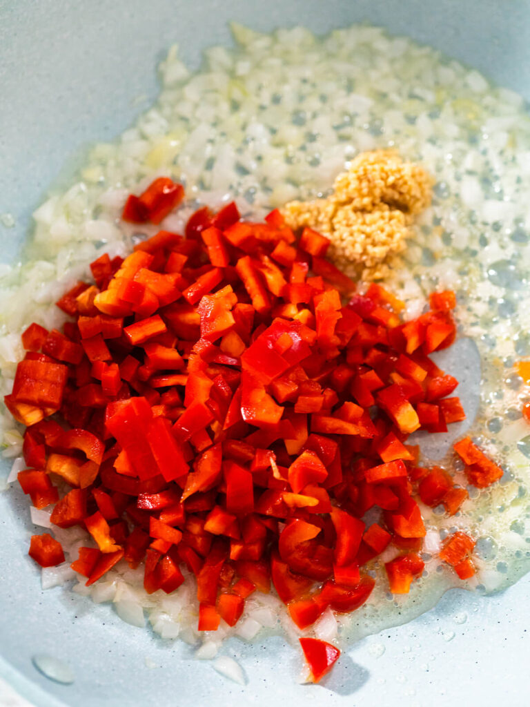 Fein gewürfelte rote Paprika, gehackter Knoblauch und glasige Zwiebelwürfel in Olivenöl in der Pfanne